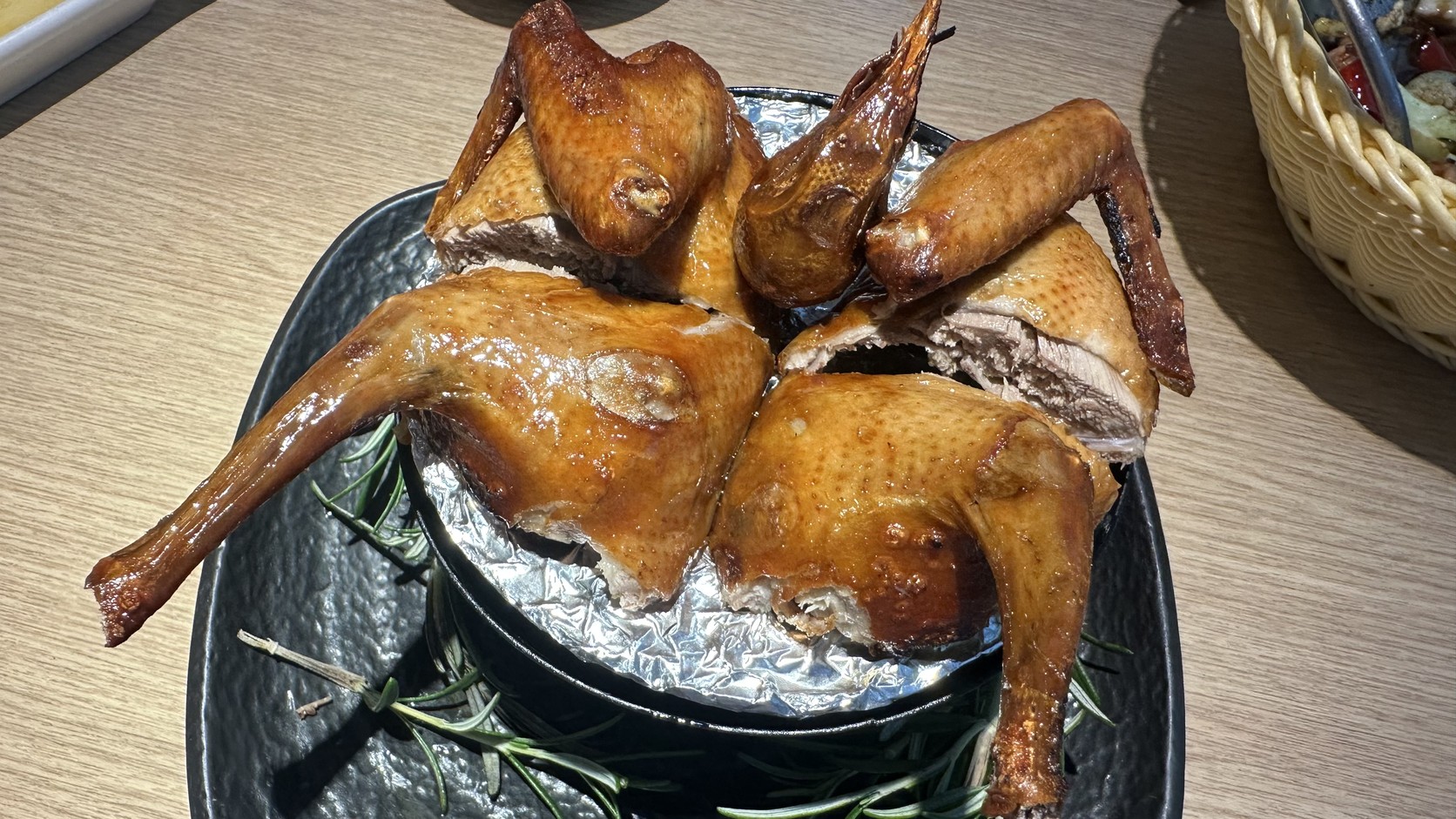 剪切後盛盤的火焰脆皮乳鴿實拍，黑色餐盤上墊著鋁箔並以迷迭香點綴