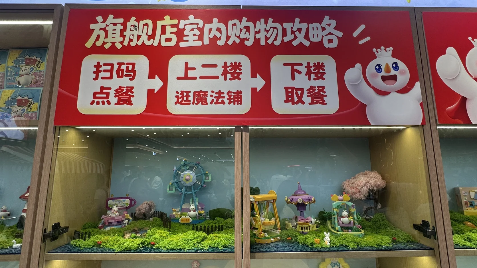 旗艦店室內購物攻略立牌：掃碼點餐、上二樓逛魔法鋪、下樓取餐三個步驟，下方為積木展示