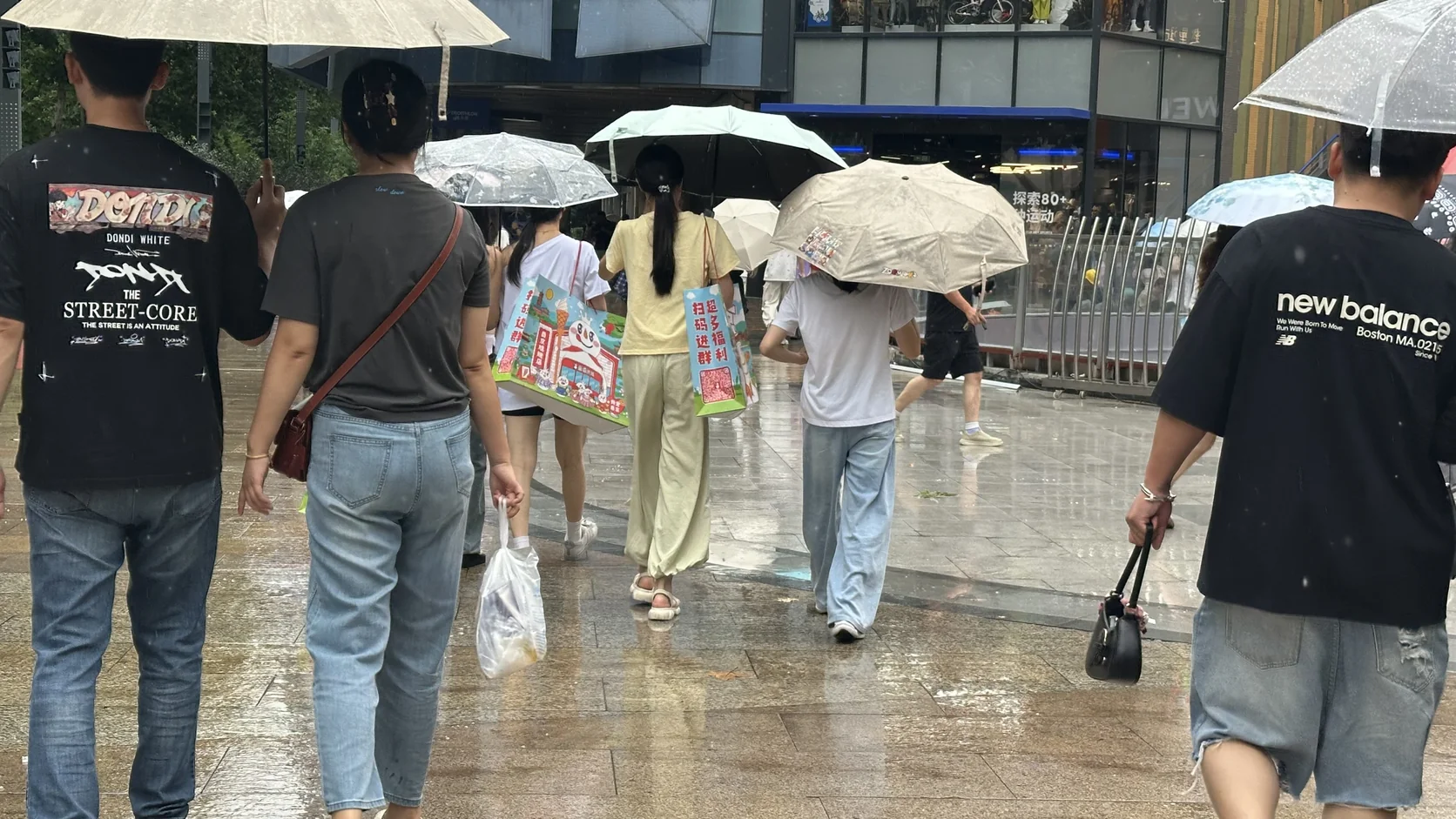 雨天的南京夫子廟街頭，路人撐著傘，有人手上提著雪王購物袋（僅背影）