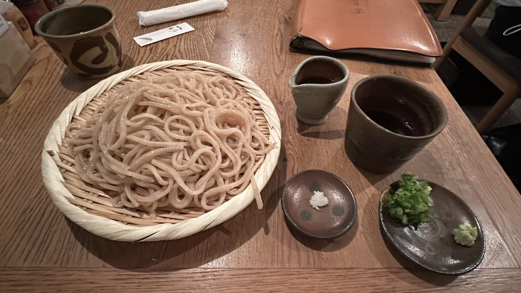 掀開蓋子後的餐桌：沾汁大杯、小壺、鹽碟，以及蔥花與山葵小碟，竹簾上的冷烏龍麵放在一旁