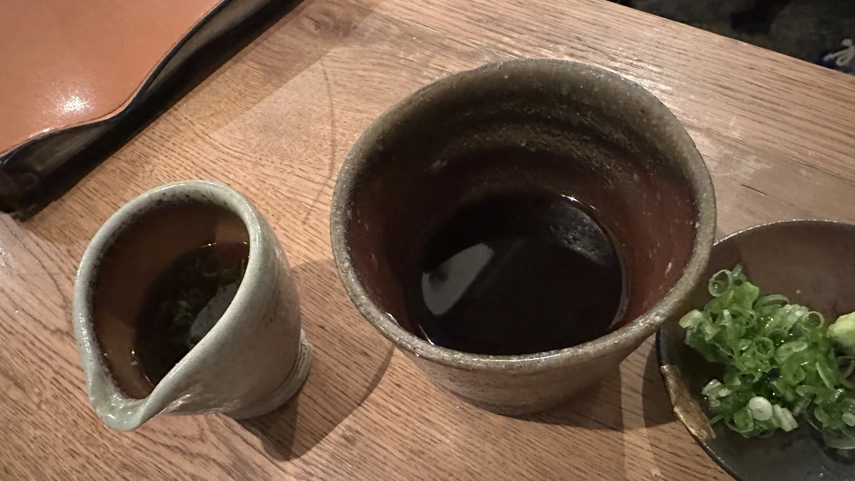 沾汁大杯與小壺近拍：大杯裝著深色沾汁，小壺裡是少量帶醬油味的冰涼液體