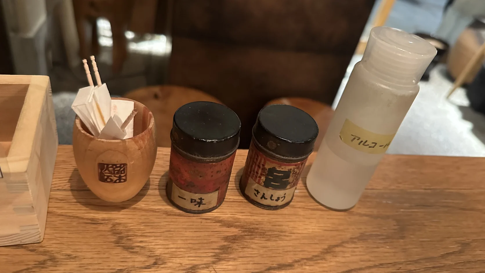 餐桌上的調味料：木桶裡的牙籤、「一味」與「さんしょう」兩個罐子，以及貼著「アルコール」標籤的小瓶
