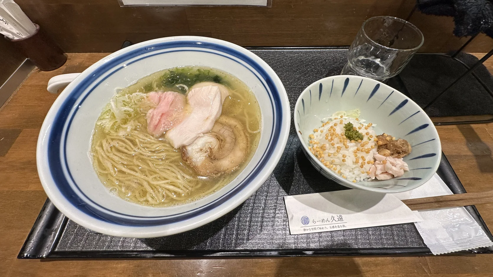 托盤上左邊是鹽味拉麵，有細麵、三種肉片與海苔；右邊小碗是白飯、黃色米果、碎肉與少許綠色佐料