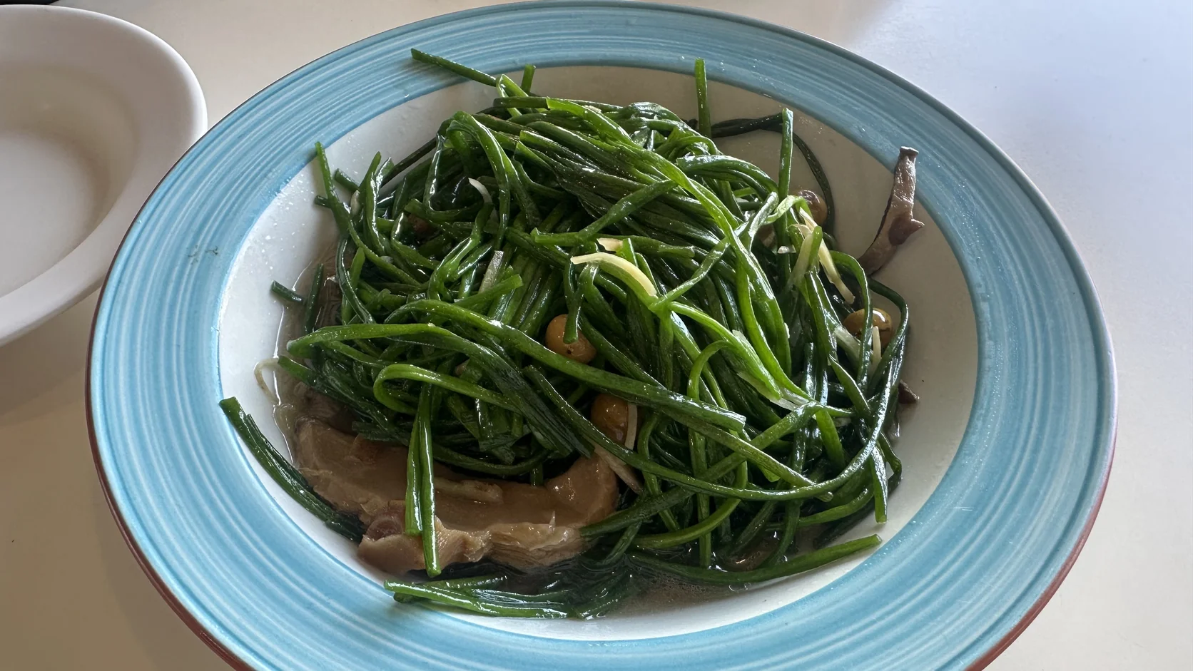 水蓮熱炒：細長翠綠的水蓮搭配菇類與蒜片，盤底有一層炒鍋油汁