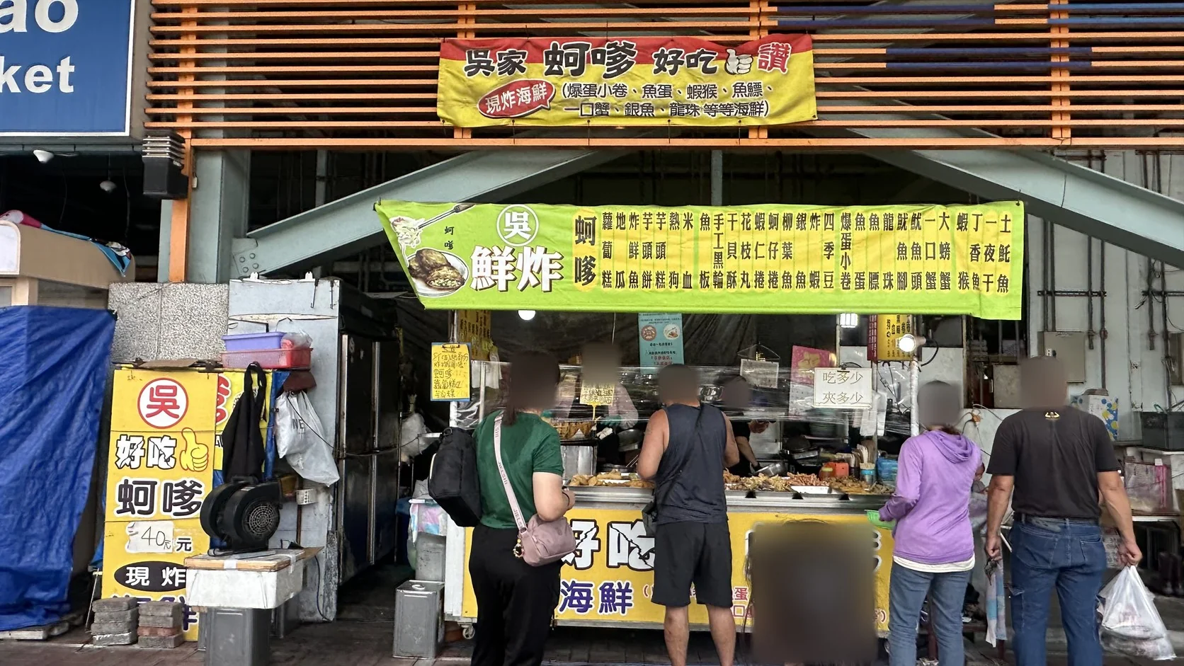 蚵仔寮魚市場旁的吳家鮮炸攤位，招牌寫著現炸海鮮，價牌標示蚵嗲一個40元，攤前有顧客排隊