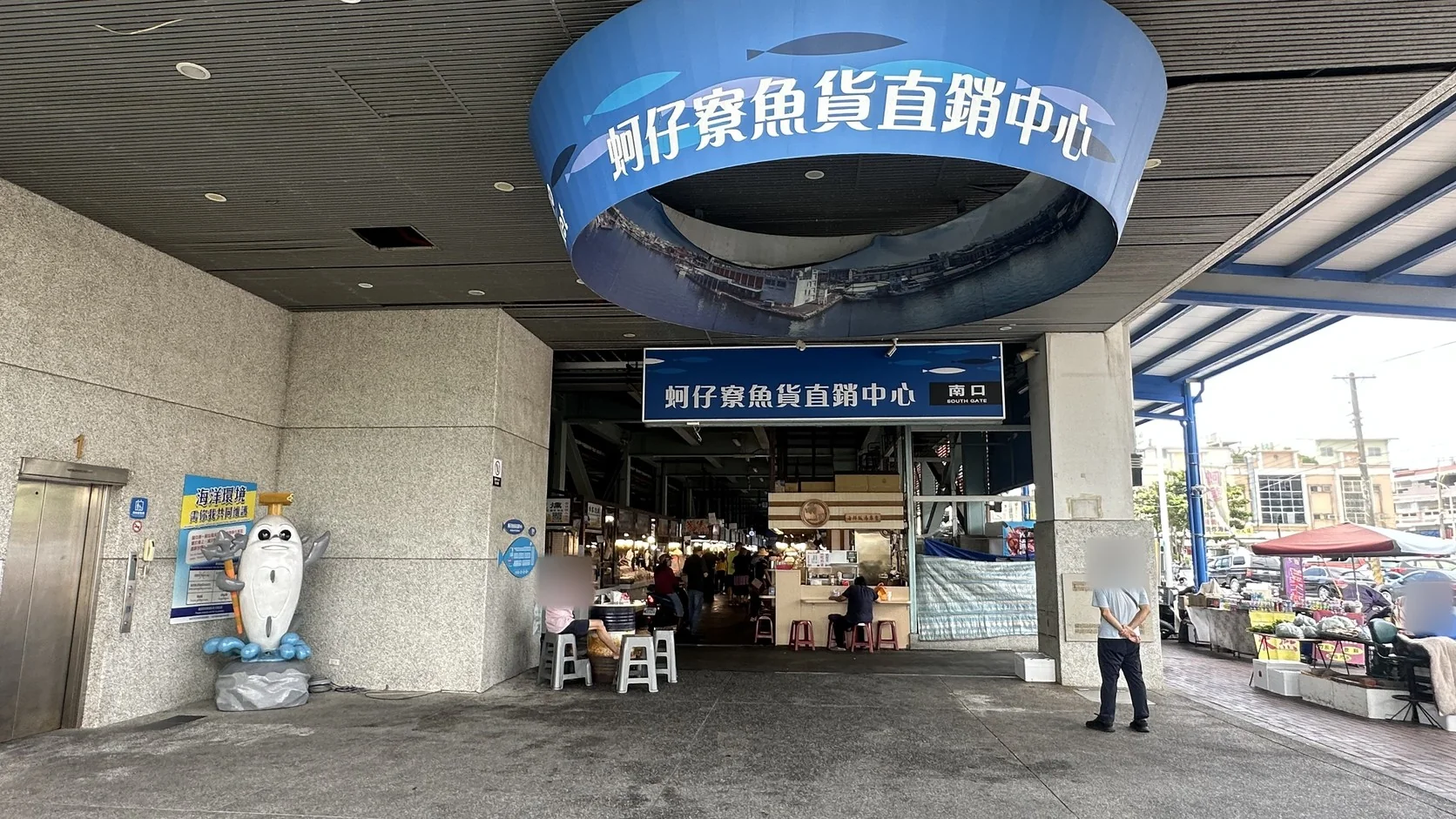 蚵仔寮魚貨直銷中心南口入口，上方圓環招牌寫著「蚵仔寮魚貨直銷中心」，入口內側可見熟食座位