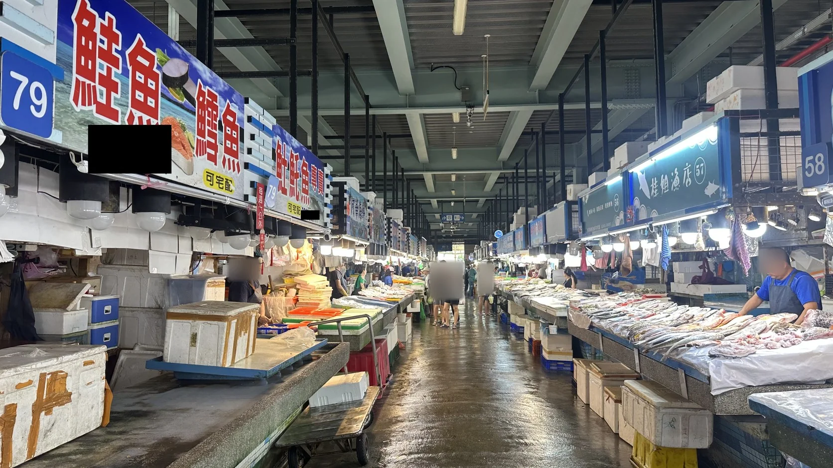 直銷中心主走道兩側的魚貨攤位已經開張，地面潮濕，攤位招牌排列在走道上方