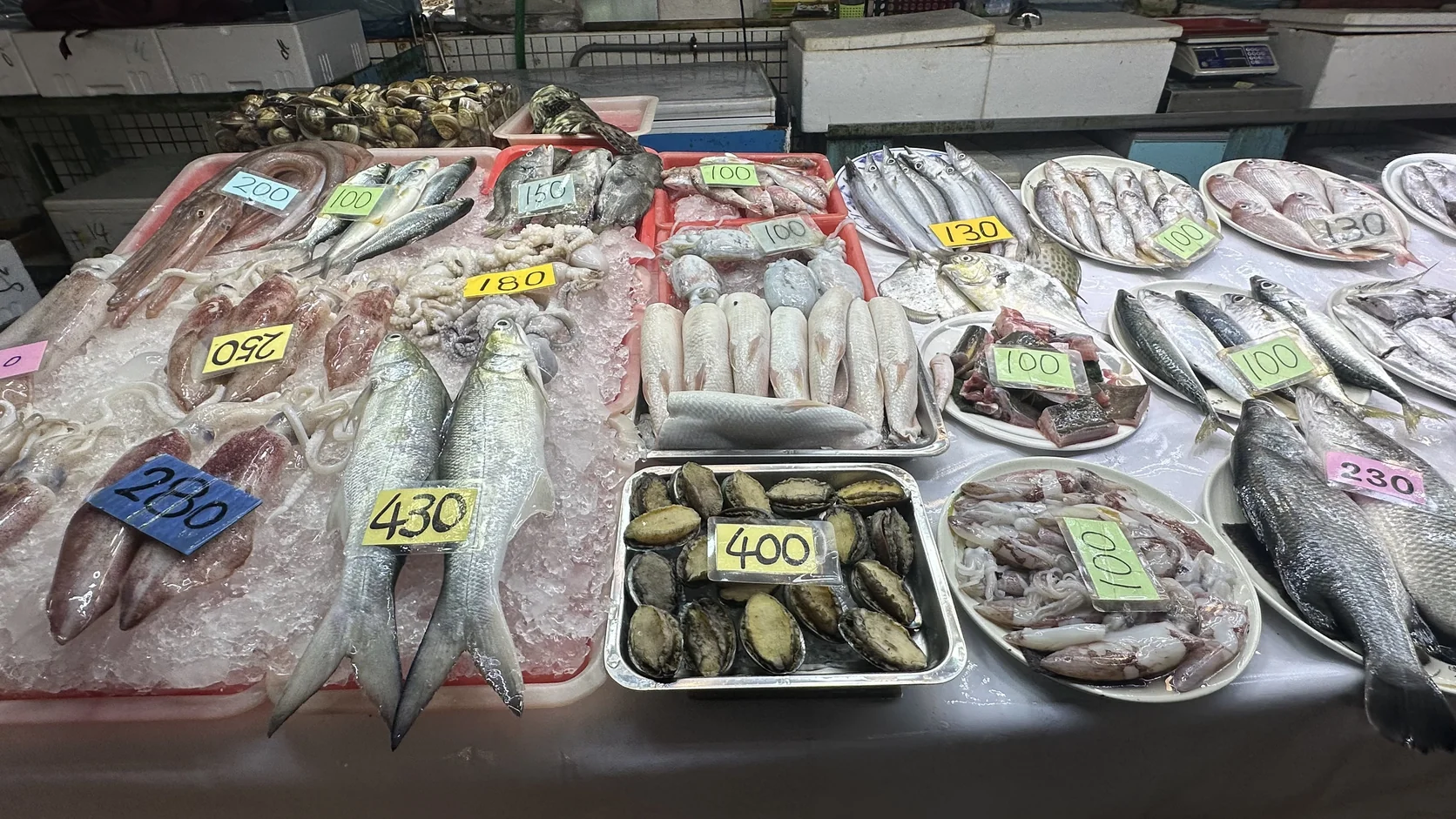 攤位上分盤陳列的魚貨與手寫價牌，價牌只標示數字，沒有標示計價單位