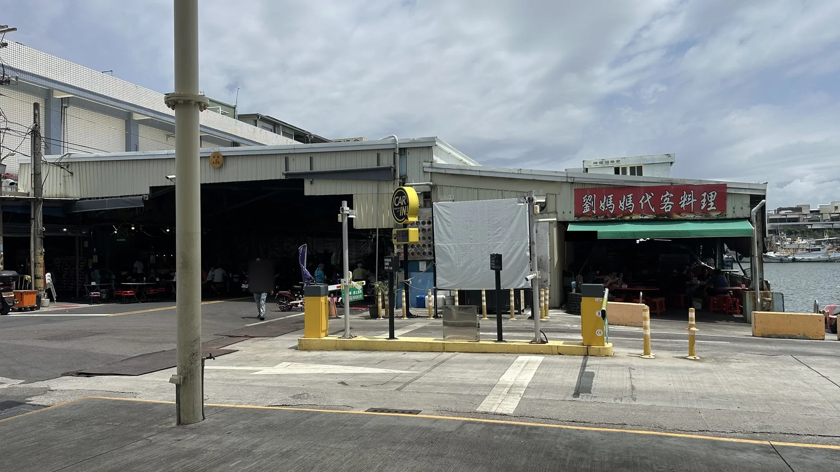 劉媽媽代客料理的紅色招牌與港邊座位區，旁邊是車道出入口閘門