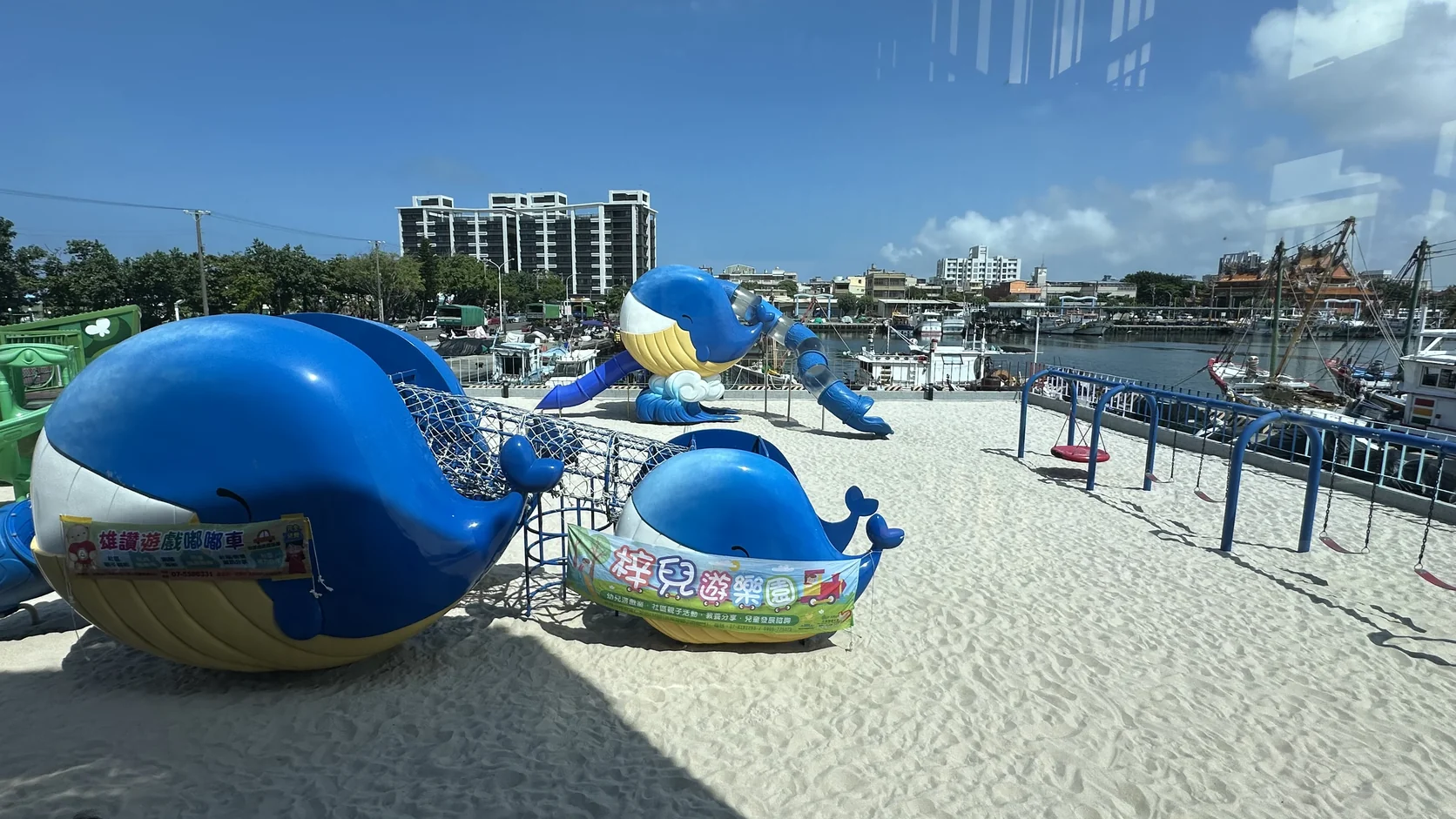 海洋教室戶外沙池與藍色鯨魚造型遊具，後方是港邊的漁港景色