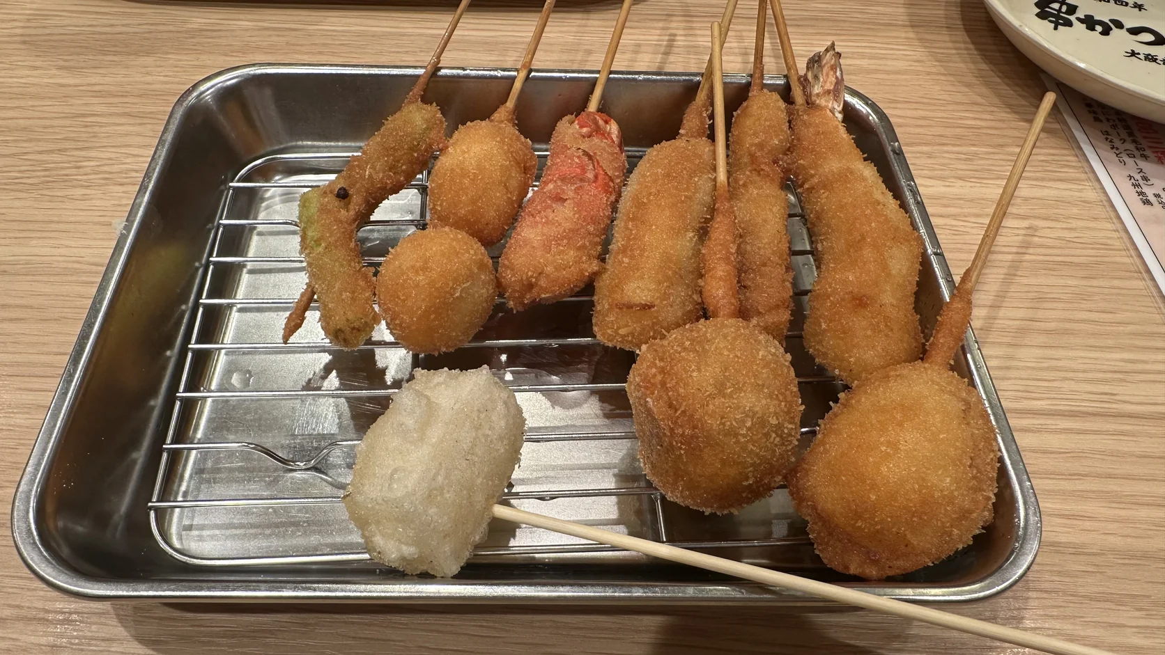 道頓堀套餐九串炸物放在鐵盤網架上的實物，麻糬一串在前方，其餘串炸都裹著金黃麵衣