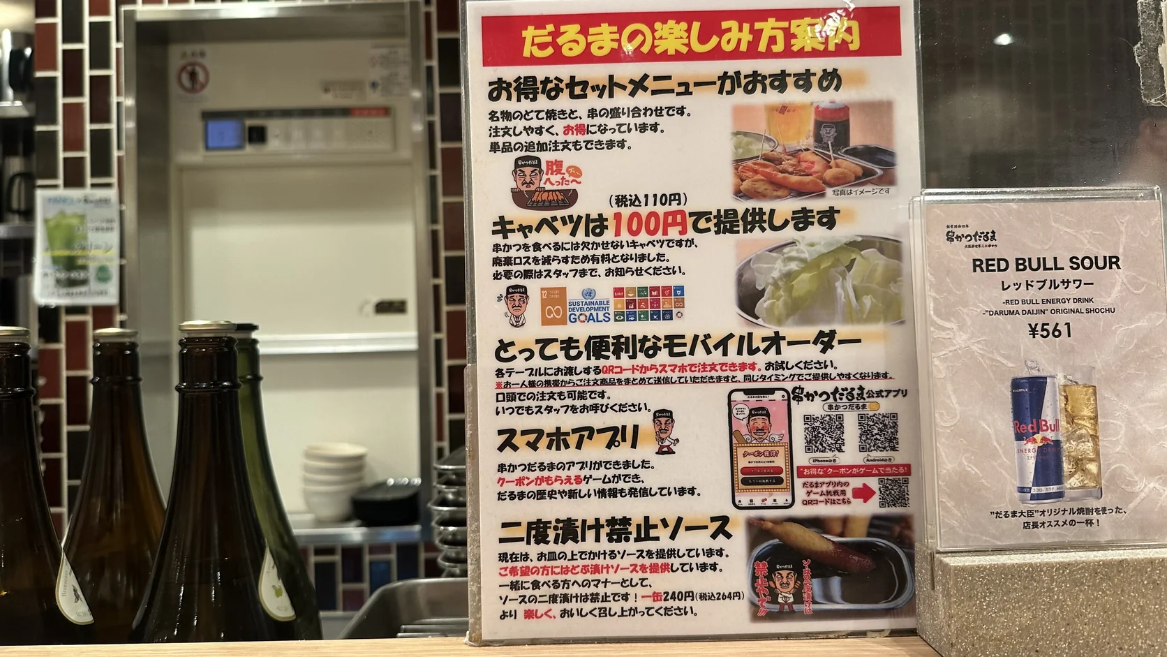 串かつだるま桌上的說明牌，介紹套餐、高麗菜加點、手機點餐、官方App，以及二度漬け禁止醬汁與沾醬價格