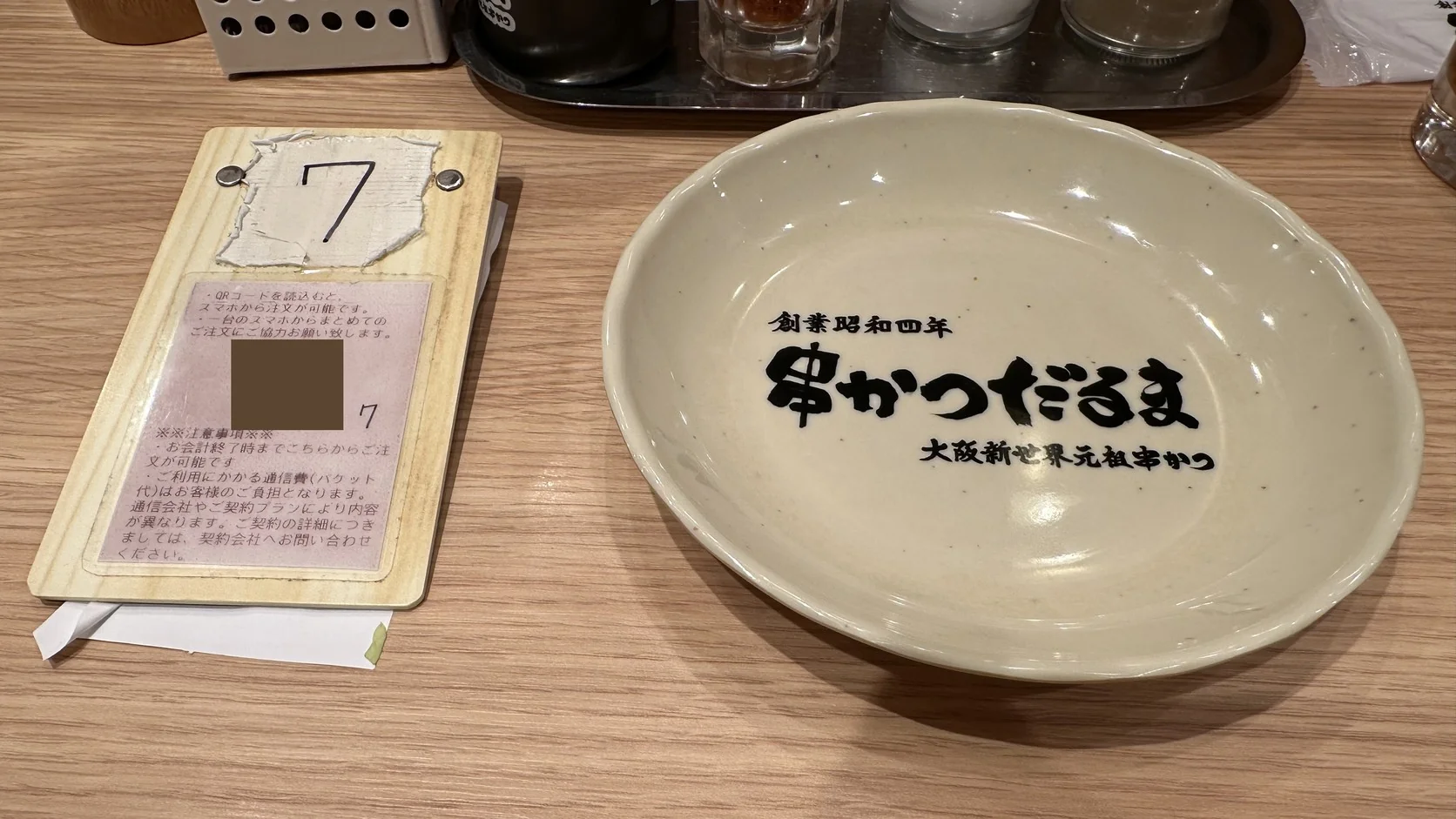 串かつだるま桌上的桌號牌與手機點餐說明（QR Code已遮蔽），旁邊是個人小盤