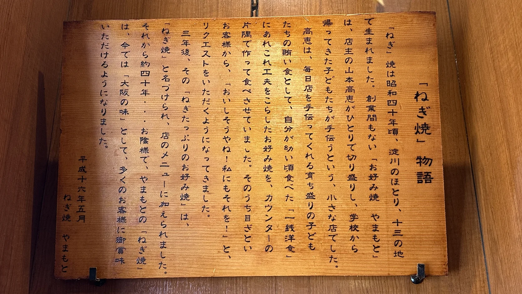店內木牌「ねぎ焼」物語，用日文寫下蔥燒誕生於十三的由來，落款是平成十六年五月