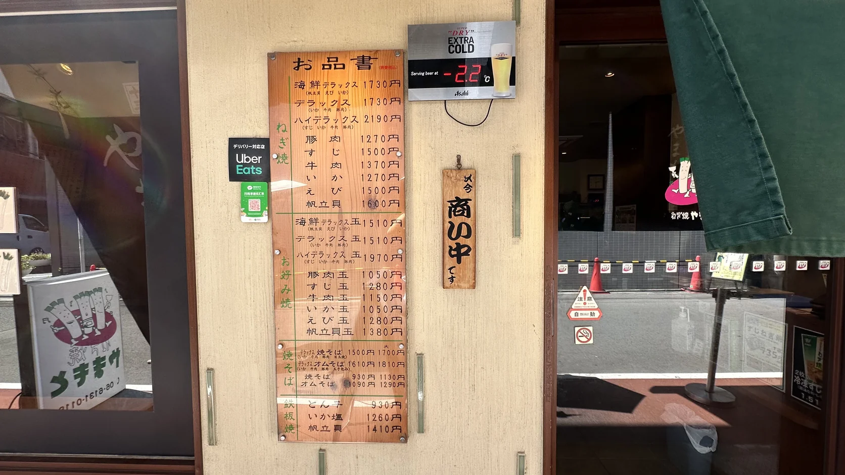 店門旁的木製價目表「お品書」，以日文列出蔥燒、大阪燒、炒麵與鐵板燒的價格