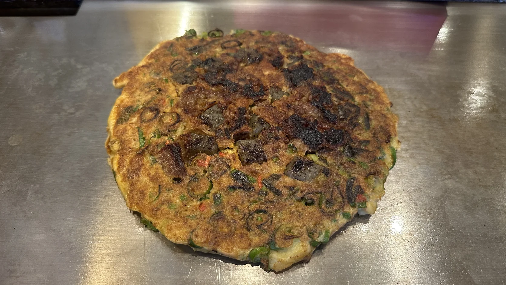 鐵板上的牛筋蔥燒全貌，表面可見大量青蔥、金黃的餅體與煎得較深的部位