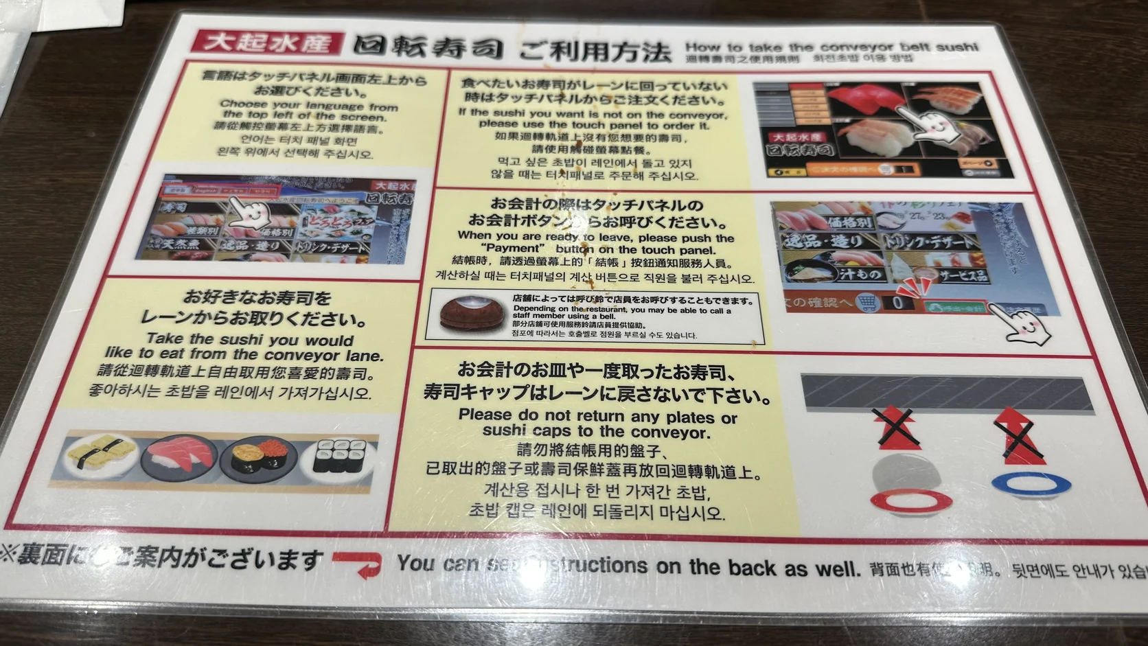 桌上的雙面迴轉壽司使用說明，有日文、繁體中文、英文與韓文，說明平板點餐與結帳方式