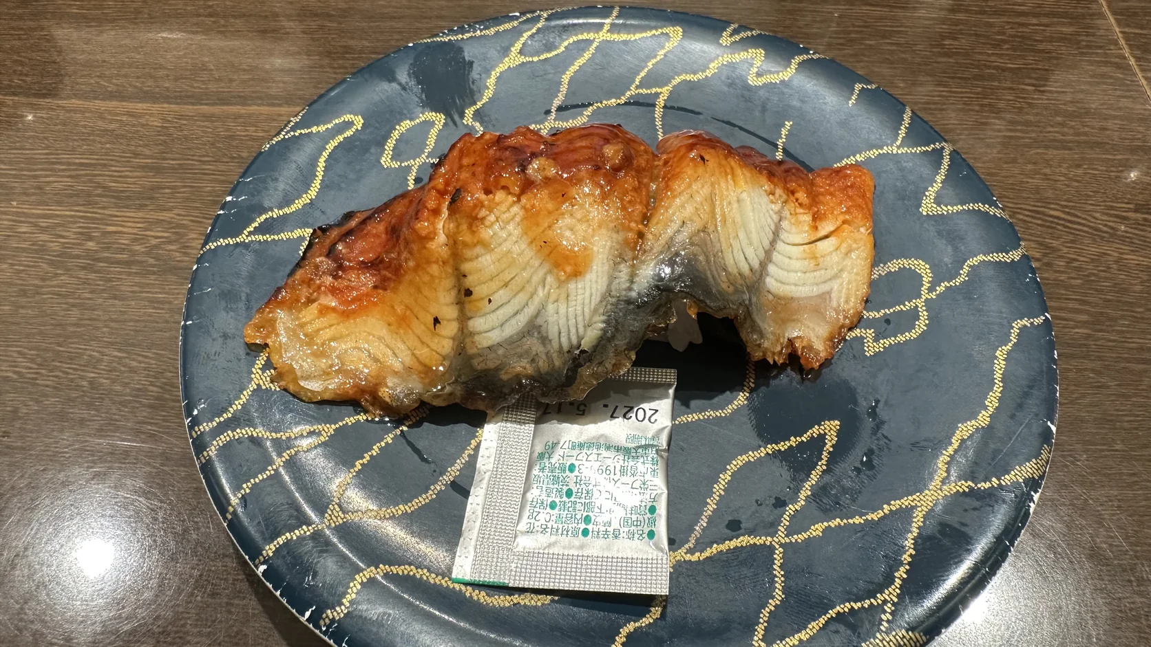 特大鰻魚握壽司，一大片鰻魚覆蓋小團醋飯，盤子旁邊附著一小包山椒粉