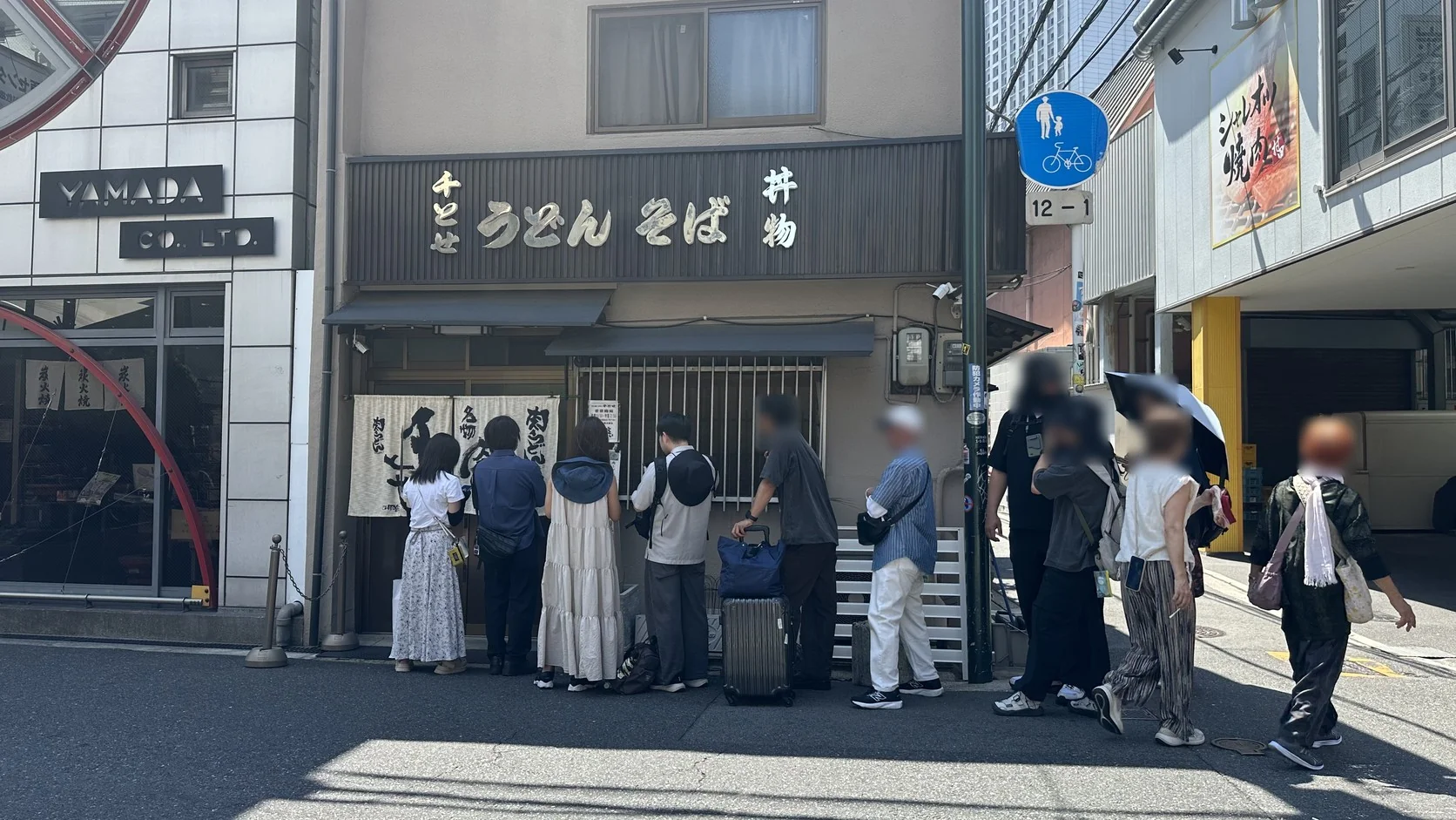 千とせ本店門口約十位客人排隊，有人拖著行李箱、有人撐傘，人物臉部已做模糊處理