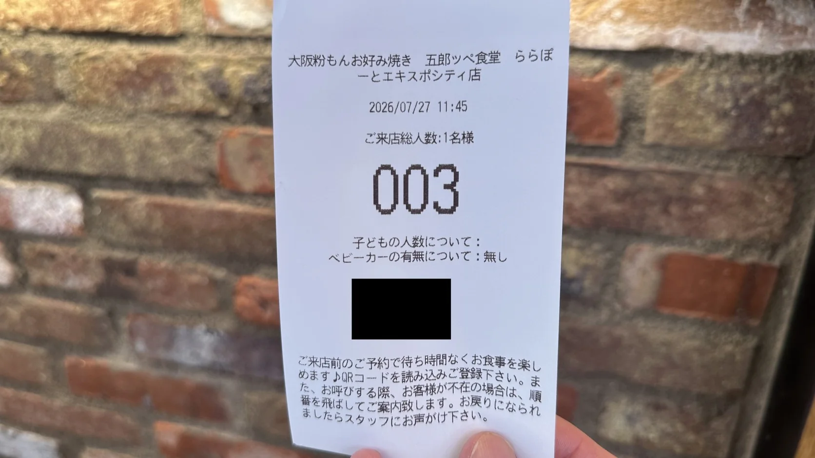 候位機印出的號碼券，上面有店名、用餐人數與候位號碼，QR Code 已遮蔽