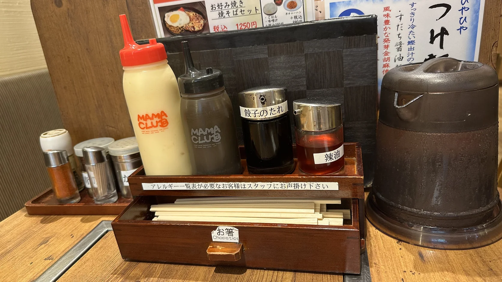 桌上的調味料與筷子盒，有黃色與黑色擠壓瓶、餃子のたれ、辣油，右側是冰水壺