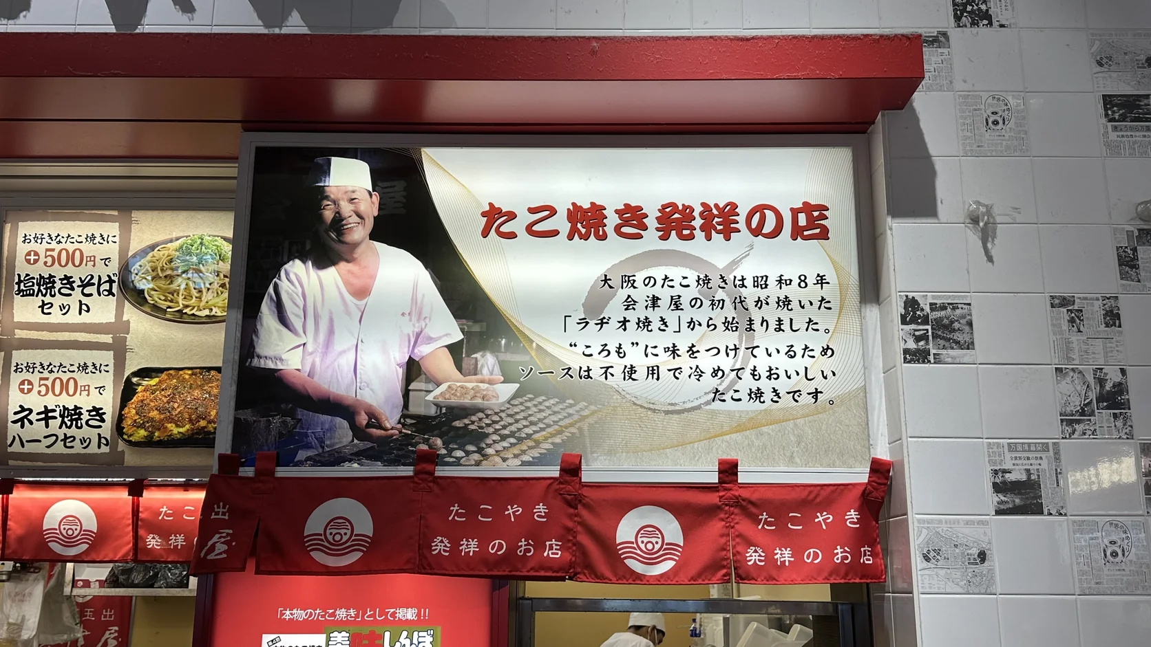 會津屋店內「たこ焼き発祥の店」看板，寫著大阪的章魚燒從昭和 8 年會津屋初代所燒的「ラヂオ焼き」開始，麵糊已調味、不使用醬汁，冷了也好吃